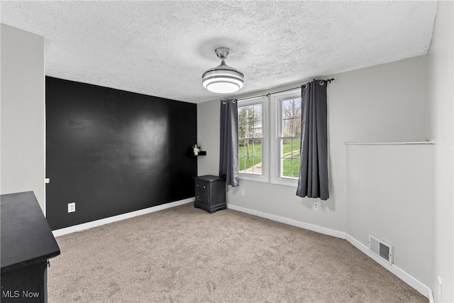 carpeted empty room featuring visible vents, a textured ceiling, and baseboards