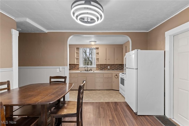 kitchen with white appliances, light countertops, arched walkways, a sink, and wood finished floors