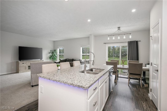 kitchen featuring white cabinetry, a sink, dark wood-style flooring, light stone countertops, and a center island with sink
