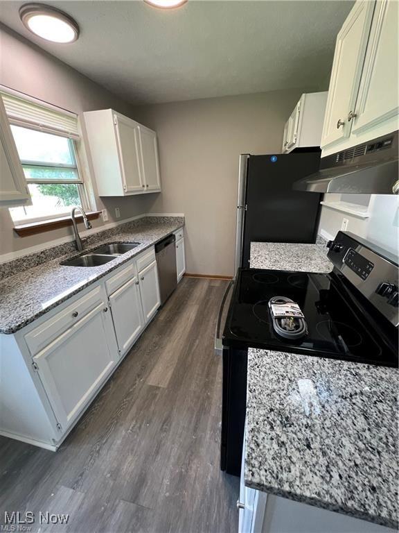 kitchen featuring appliances with stainless steel finishes, white cabinetry, under cabinet range hood, dark wood finished floors, and a sink