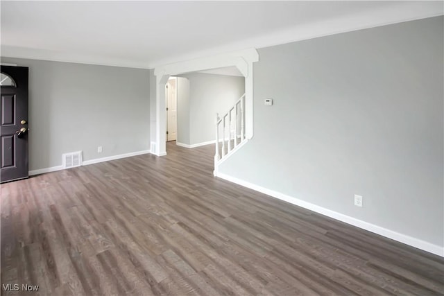 unfurnished living room with visible vents, baseboards, arched walkways, stairs, and dark wood-type flooring