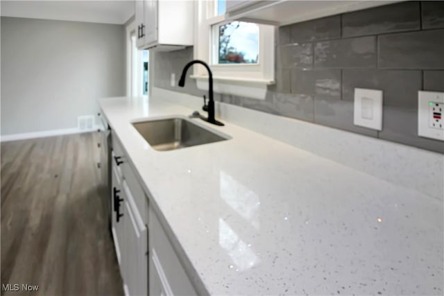 kitchen featuring tasteful backsplash, white cabinets, baseboards, a sink, and wood finished floors