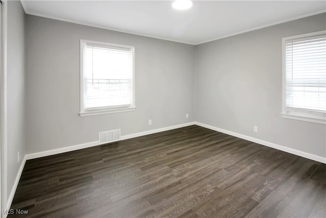 spare room with visible vents, baseboards, ornamental molding, and dark wood finished floors