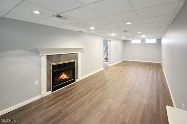 unfurnished living room with a tile fireplace, visible vents, baseboards, and wood finished floors