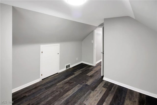 additional living space with dark wood-style flooring, visible vents, baseboards, and lofted ceiling