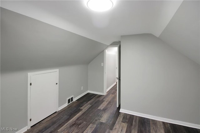 bonus room featuring baseboards, lofted ceiling, dark wood-style floors, and visible vents