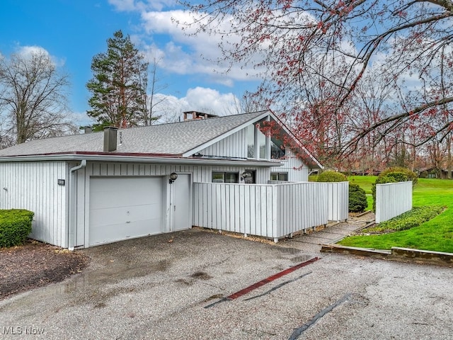 exterior space featuring driveway, a shingled roof, a garage, and fence