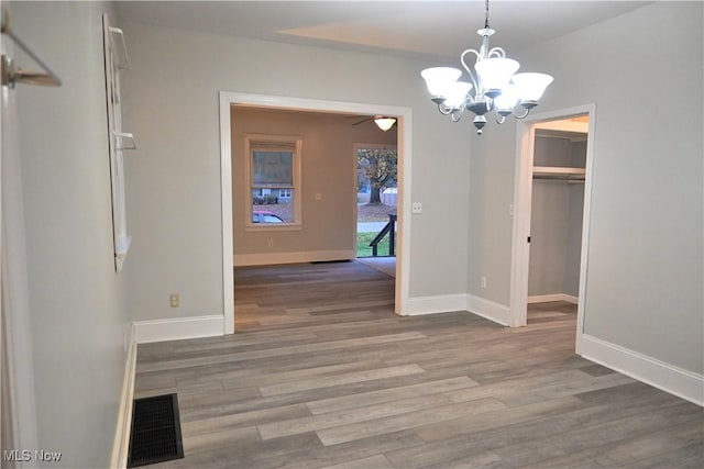 unfurnished dining area featuring visible vents, baseboards, wood finished floors, and ceiling fan with notable chandelier