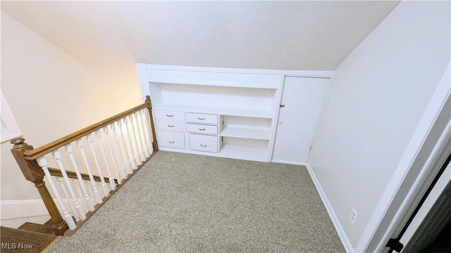 interior space with baseboards, an upstairs landing, light carpet, and a textured ceiling