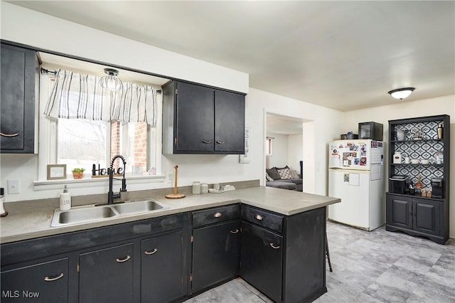 kitchen with freestanding refrigerator, a peninsula, a sink, light countertops, and dark cabinetry