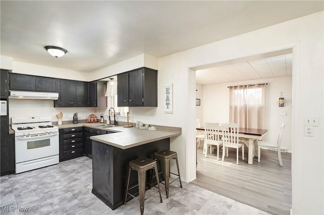 kitchen featuring white gas range oven, a peninsula, under cabinet range hood, a sink, and a breakfast bar area