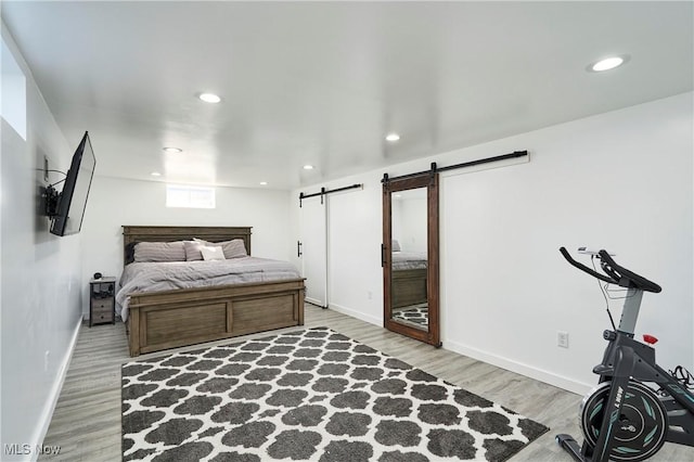 bedroom with a barn door, baseboards, wood finished floors, and recessed lighting