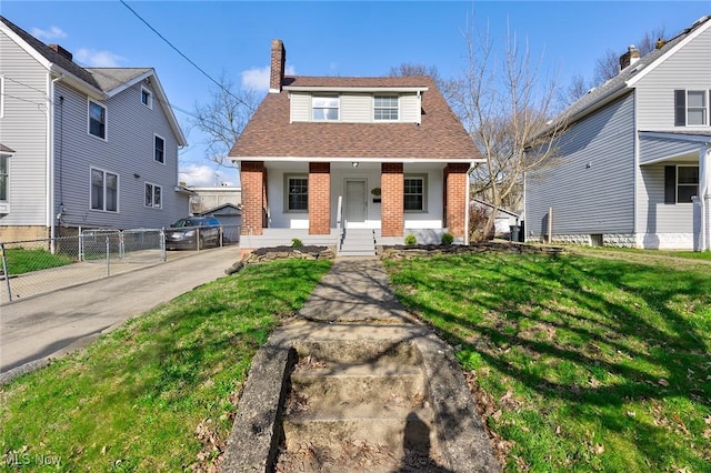 view of front of house featuring roof with shingles, a chimney, a front lawn, brick siding, and fence