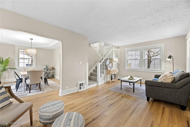 living area with light wood-style flooring, arched walkways, visible vents, stairs, and baseboards