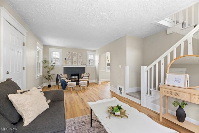 living area with a textured ceiling, stairway, wood finished floors, and a fireplace