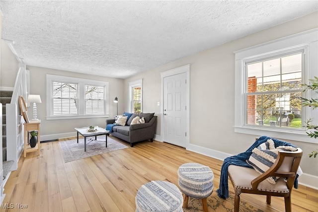 living room with stairway, light wood-type flooring, a textured ceiling, and baseboards