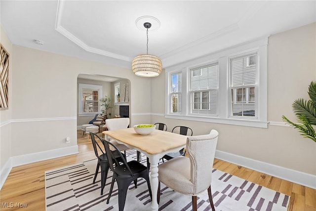 dining space with a tray ceiling, arched walkways, baseboards, and light wood-style floors
