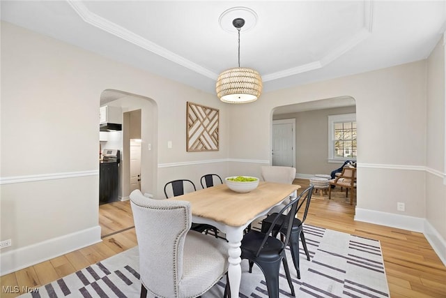 dining space featuring a tray ceiling, arched walkways, baseboards, and light wood-type flooring