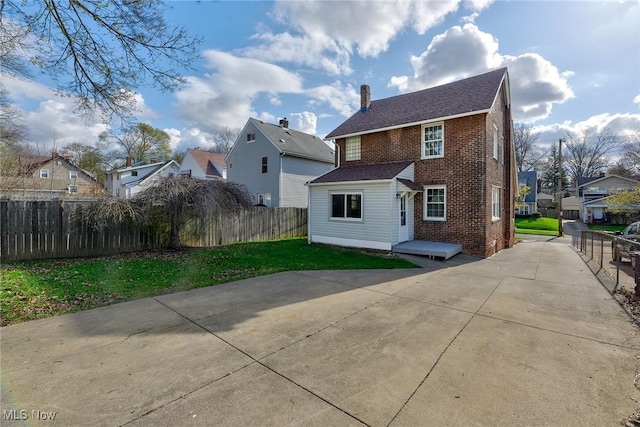 back of property with brick siding, fence, a residential view, and a chimney