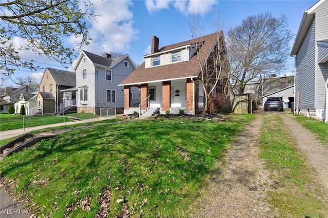 view of front of property featuring a front yard, covered porch, a chimney, brick siding, and a residential view