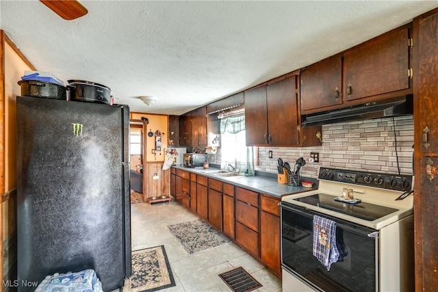 kitchen with freestanding refrigerator, under cabinet range hood, visible vents, range with electric cooktop, and decorative backsplash