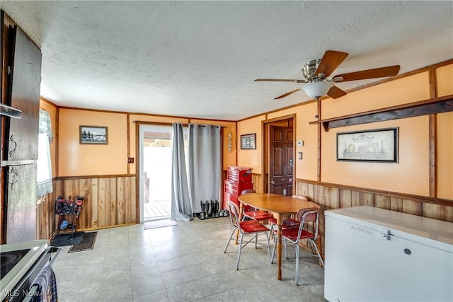 dining room with a textured ceiling, wood walls, ceiling fan, and wainscoting