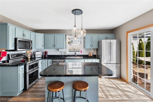 kitchen featuring a kitchen bar, decorative backsplash, a sink, stainless steel appliances, and light wood finished floors