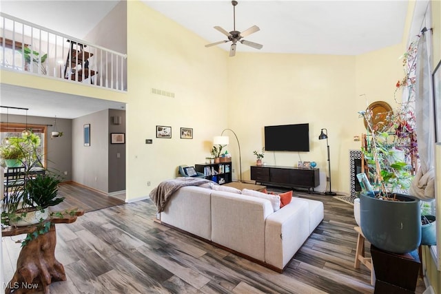 living room with a towering ceiling, baseboards, a ceiling fan, visible vents, and wood finished floors