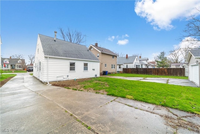 back of property featuring concrete driveway, a residential view, fence, and a lawn