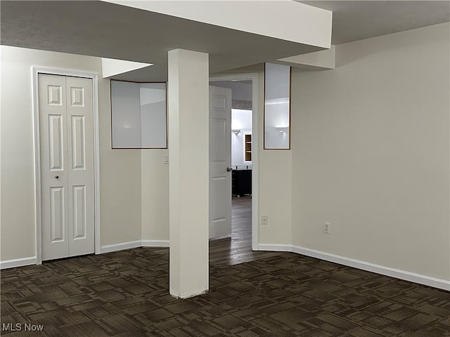 below grade area featuring dark carpet and baseboards