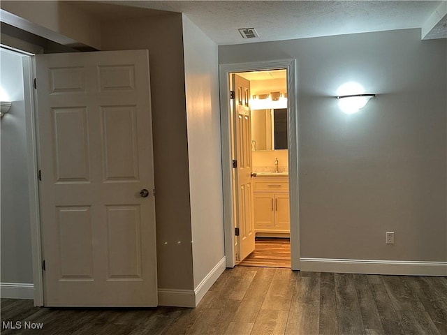 unfurnished bedroom with ensuite bath, visible vents, dark wood-style flooring, a sink, and baseboards