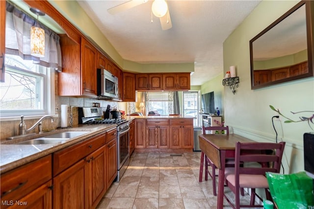 kitchen with stainless steel appliances, brown cabinets, a sink, and a ceiling fan