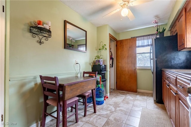 kitchen featuring brown cabinetry, freestanding refrigerator, and a ceiling fan
