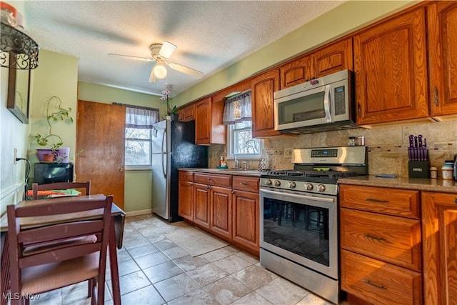 kitchen with stainless steel appliances, brown cabinets, backsplash, and a ceiling fan