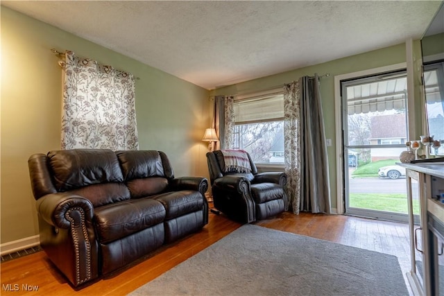 living area with a textured ceiling, wood finished floors, visible vents, and a wealth of natural light