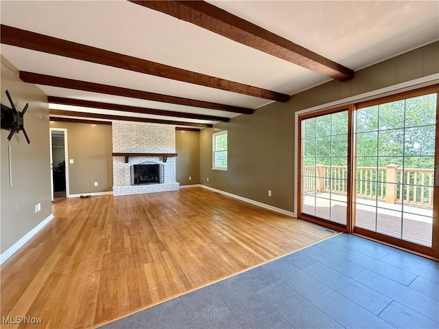 21 Ashwood Dr, Vienna, WV 26105 - unfurnished living room with beam ceiling, baseboards, a brick fireplace, and light wood-type flooring