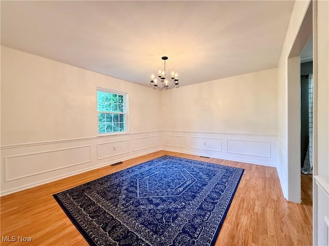 21 Ashwood Dr, Vienna, WV 26105 - unfurnished dining area with a chandelier, a decorative wall, a wainscoted wall, and wood finished floors