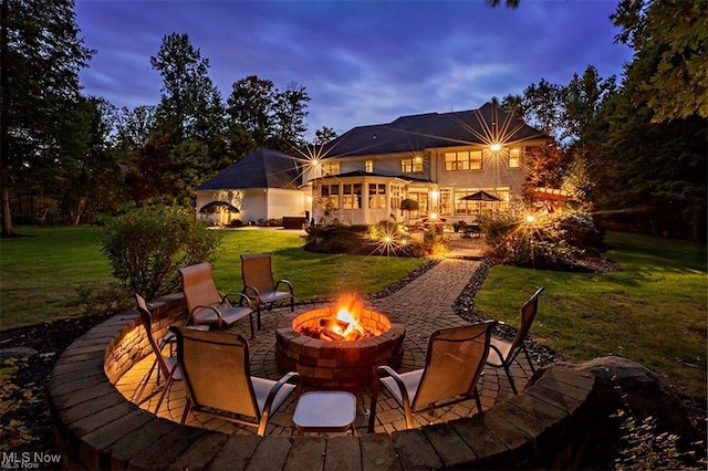 back of property at dusk with a fire pit, a patio, and a lawn