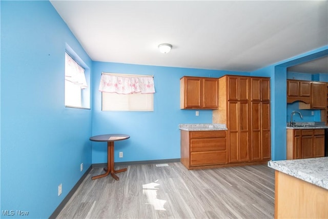 kitchen with brown cabinets, light wood-style flooring, baseboards, and a sink