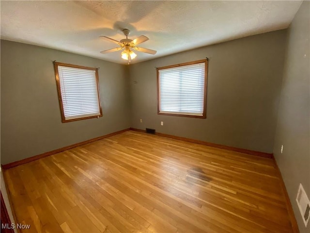 spare room with light wood-style floors, baseboards, a ceiling fan, and visible vents