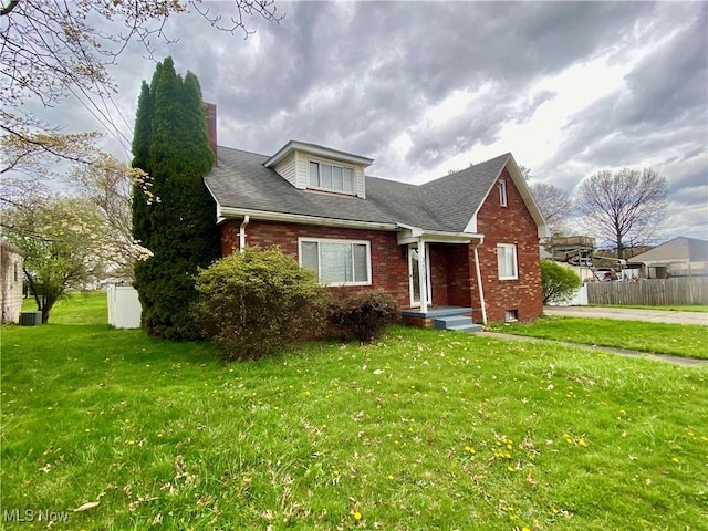 view of front of property with cooling unit, fence, a front lawn, brick siding, and a shingled roof