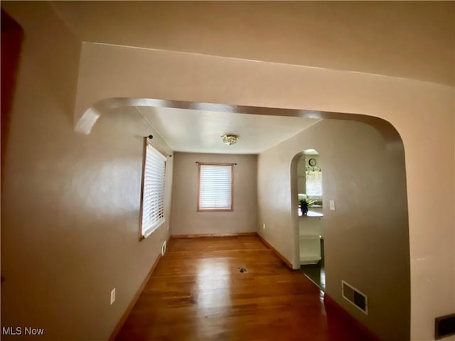 interior space featuring visible vents, baseboards, arched walkways, and wood finished floors