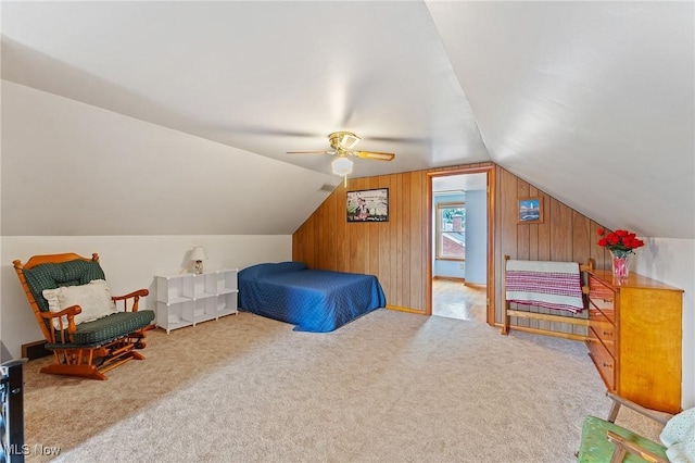 unfurnished bedroom with lofted ceiling, a ceiling fan, wooden walls, and carpet
