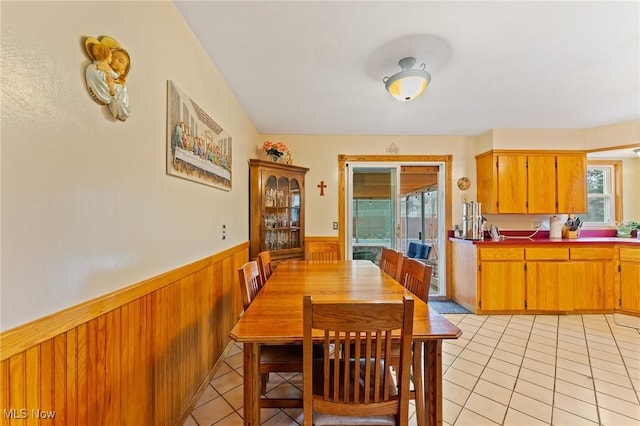 dining area with light tile patterned flooring, wood walls, and wainscoting