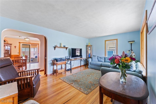 living room with arched walkways, a healthy amount of sunlight, a textured ceiling, and light wood finished floors