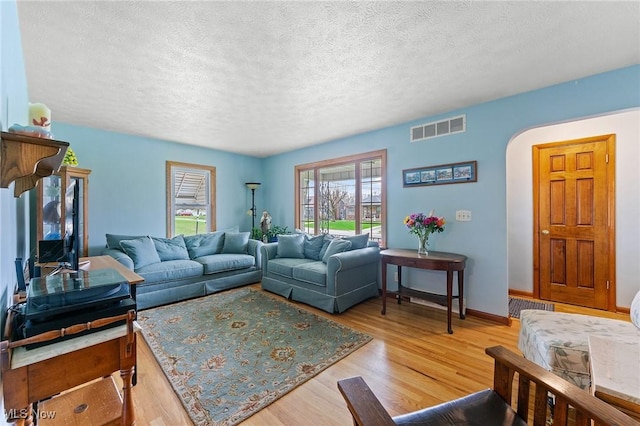 living area featuring wood finished floors, visible vents, arched walkways, baseboards, and a textured ceiling