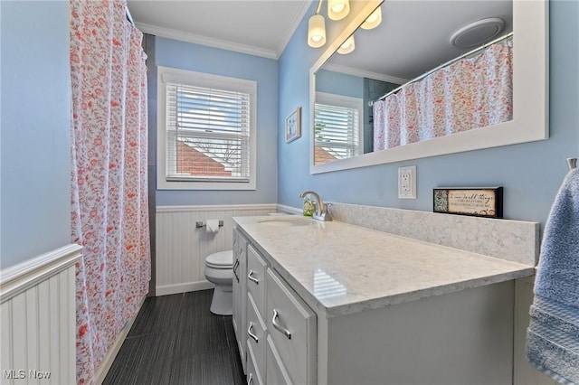 full bath featuring wainscoting, toilet, vanity, and crown molding