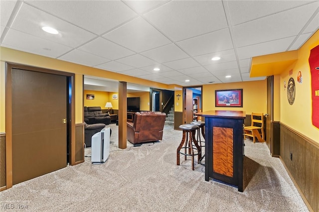interior space featuring carpet, a drop ceiling, a dry bar, and wainscoting