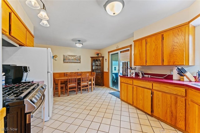kitchen with brown cabinetry, stainless steel gas stove, dark countertops, and light tile patterned floors