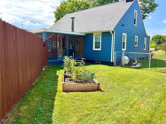 rear view of property featuring a sunroom, a vegetable garden, a lawn, and roof with shingles